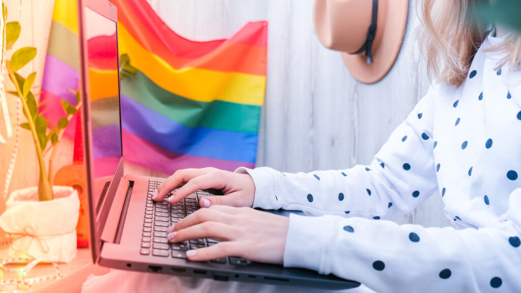 Young Millennial Hippie Woman Sitting Balcony Using Laptop Lgbtq Rainbow Flag Background 1024x576